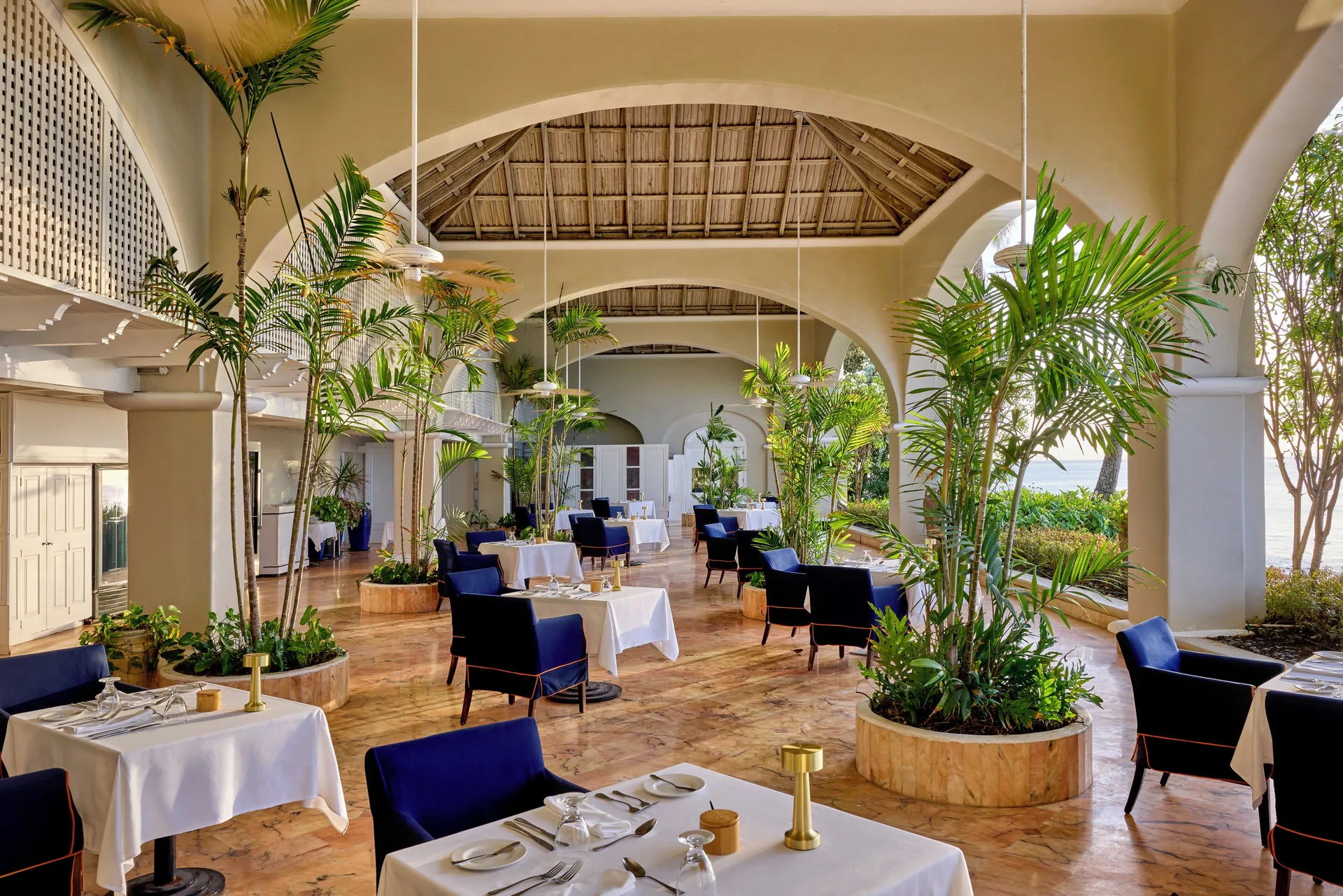 Open-air dining terrace with palms and white tablecloths at Fairmont Royal Pavilion.