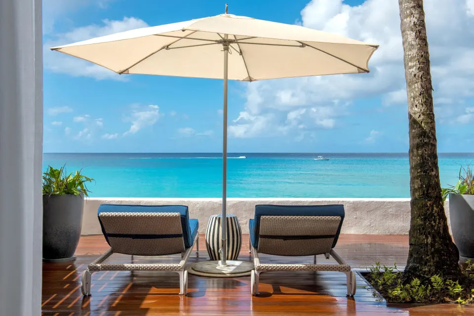 Beachfront suite terrace with two loungers under an umbrella at Fairmont Royal Pavilion.