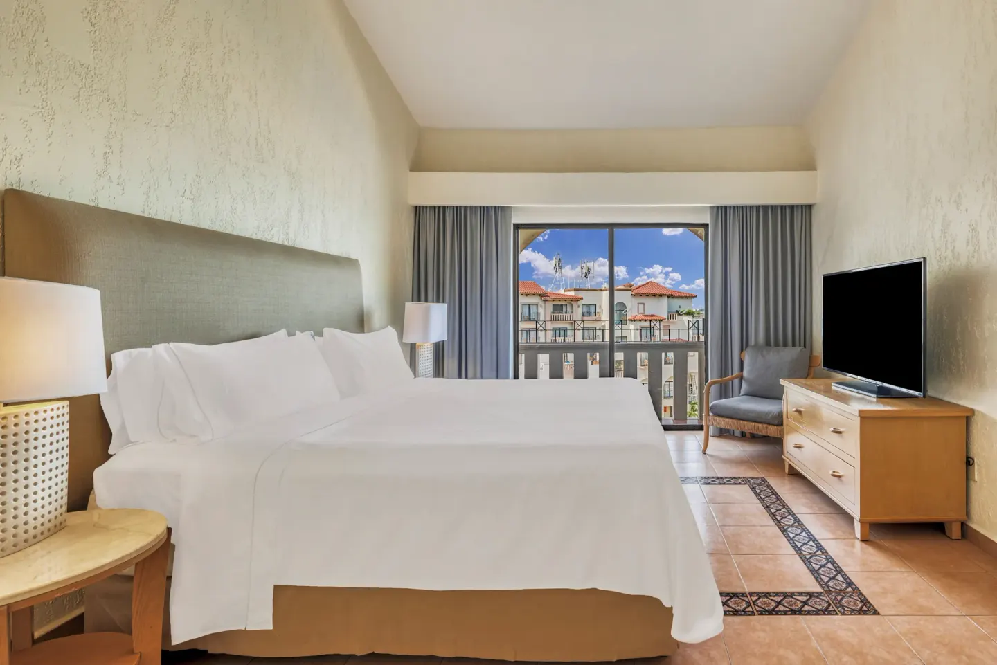King bed guest room with balcony doors and TV at Fiesta Americana Cancun Villas.