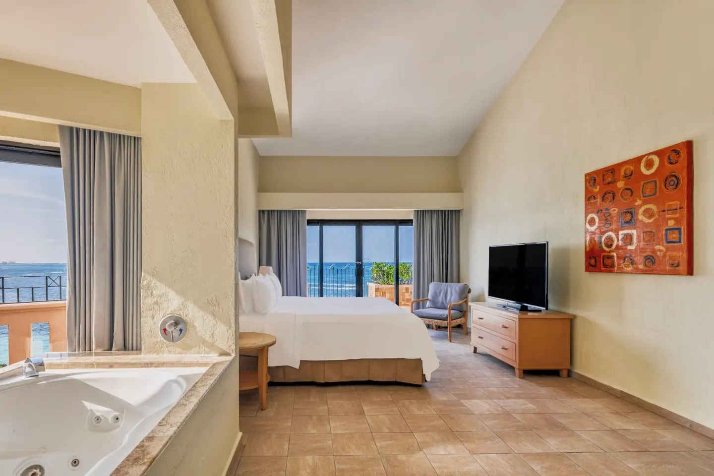 Guest room with bed, in-room tub, TV, and ocean balcony at Fiesta Americana Cancun Villas.