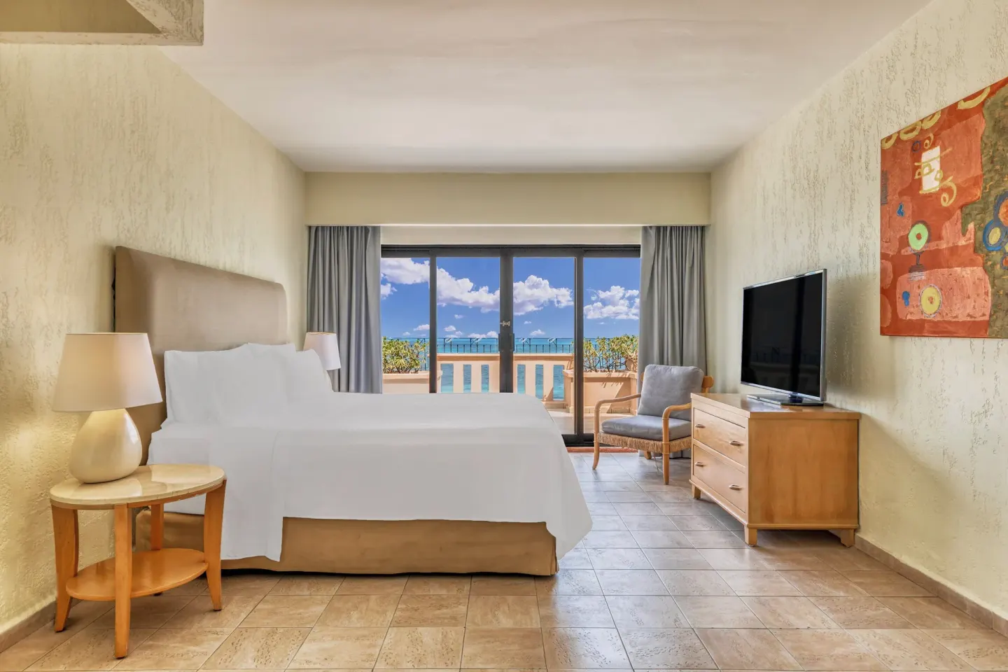 Guest room with one bed, TV, armchair, and ocean-facing balcony at Fiesta Americana Cancun Villas.