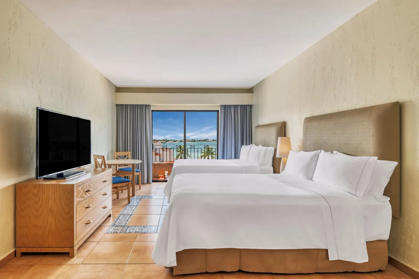 Guest room with two beds, TV, small table, and balcony view at Fiesta Americana Cancun Villas.