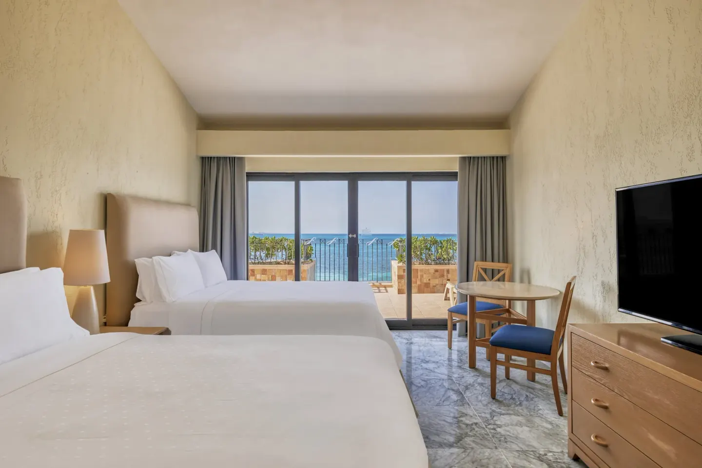 Guest room with two beds, table, TV, and ocean-facing terrace at Fiesta Americana Cancun Villas.