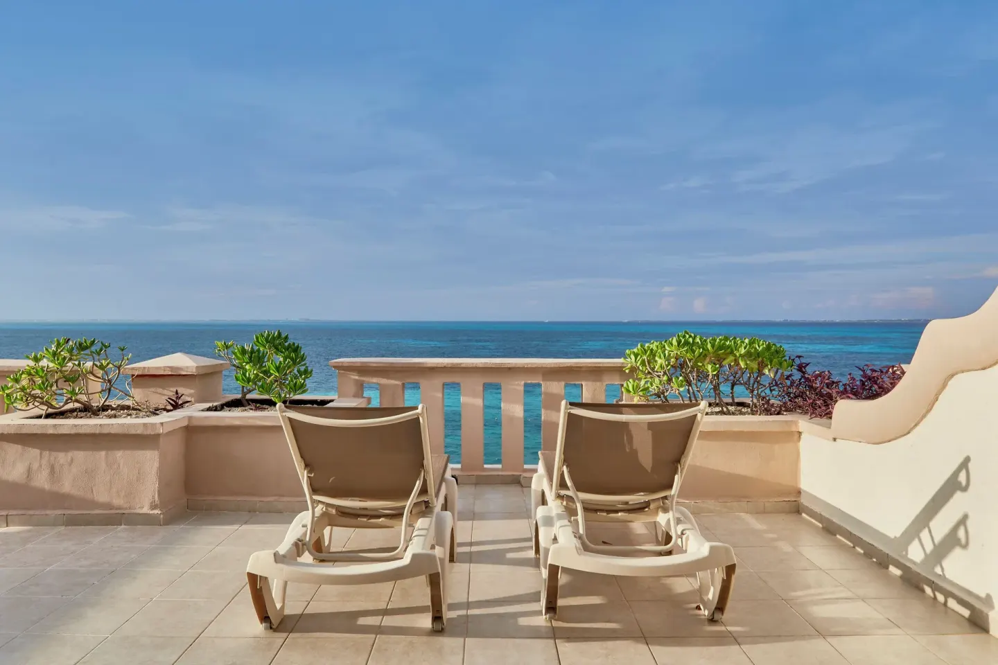 Two lounge chairs face the turquoise sea from a terrace at Fiesta Americana Cancun Villas.