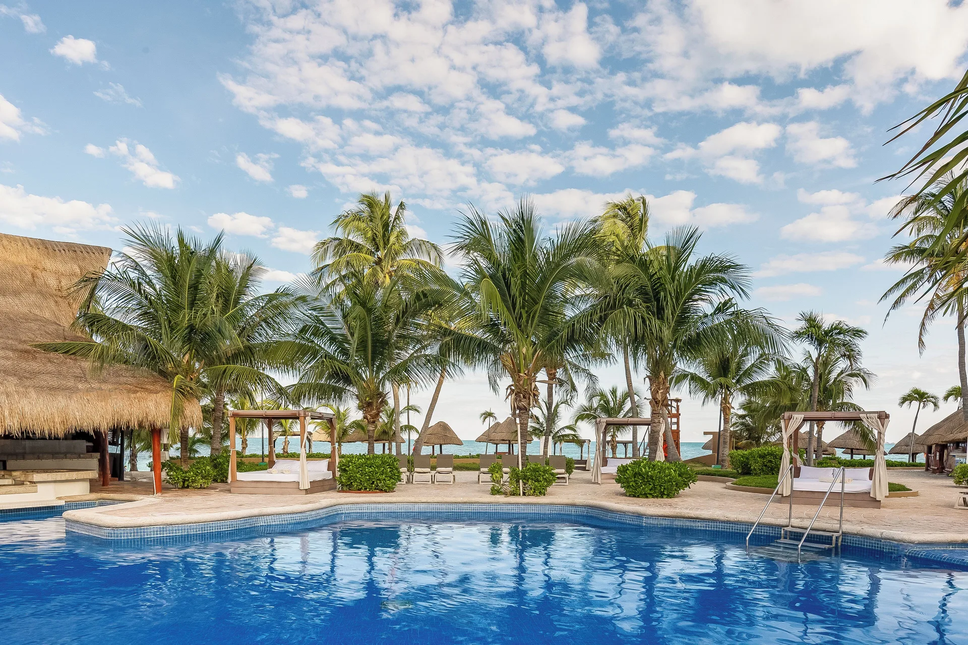 Pool, palm trees, daybeds, and ocean beyond at Fiesta Americana Cancun Villas.