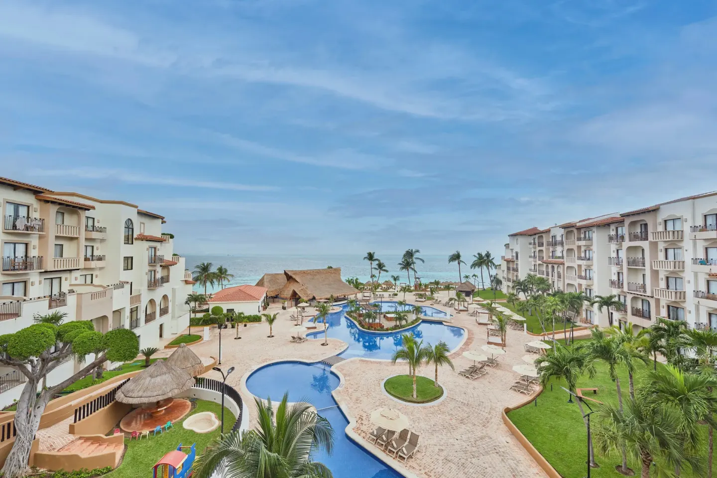 Pools, palms, and villa buildings beside the sea at Fiesta Americana Cancun Villas.