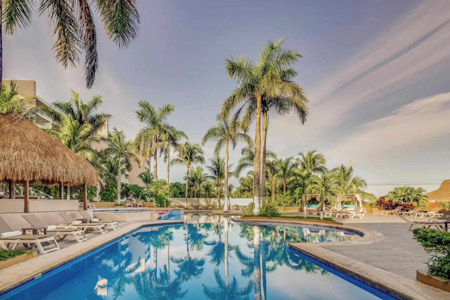 Curved resort pool with palm reflections and lounge chairs at Fiesta Americana Cozumel.