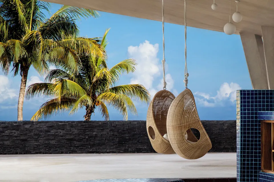 Two woven hanging chairs face palm trees and the sea at Fiesta Americana Cozumel.