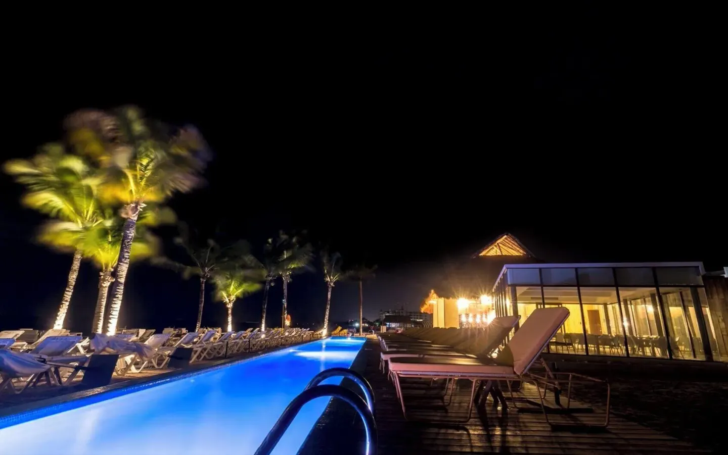 Night view of the illuminated pool, loungers, and palms at Fiesta Americana Cozumel.