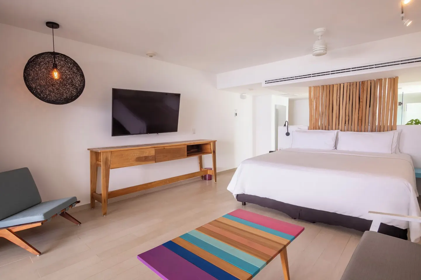 King bed guest room with TV, lounge chair, and pendant light at Fiesta Americana Cozumel.