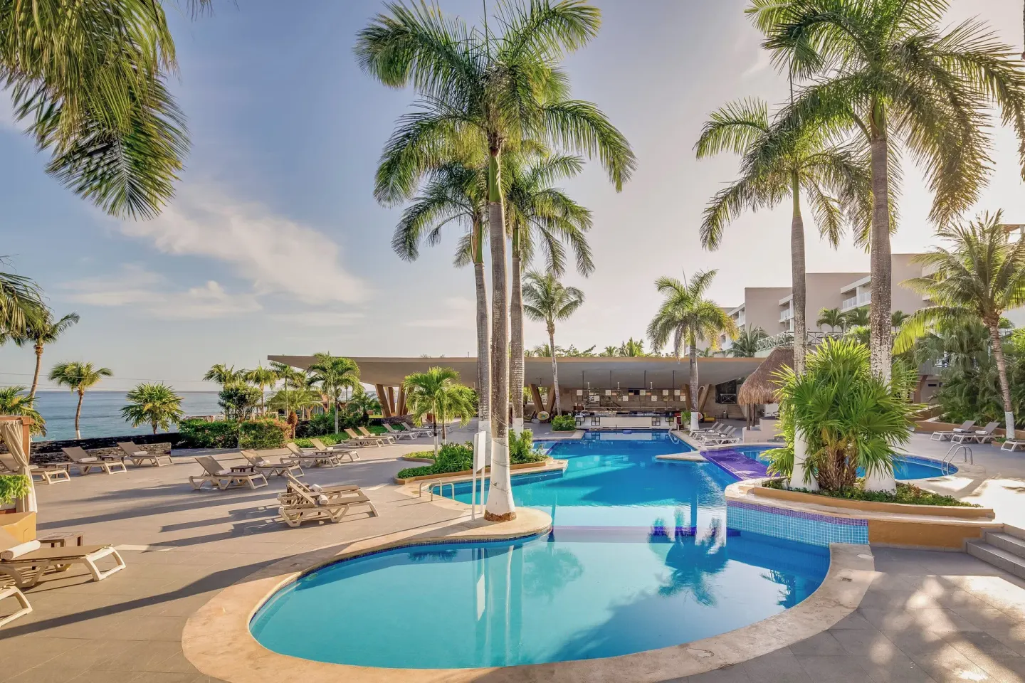 Resort pool with palm trees, loungers, and ocean beyond at Fiesta Americana Cozumel.