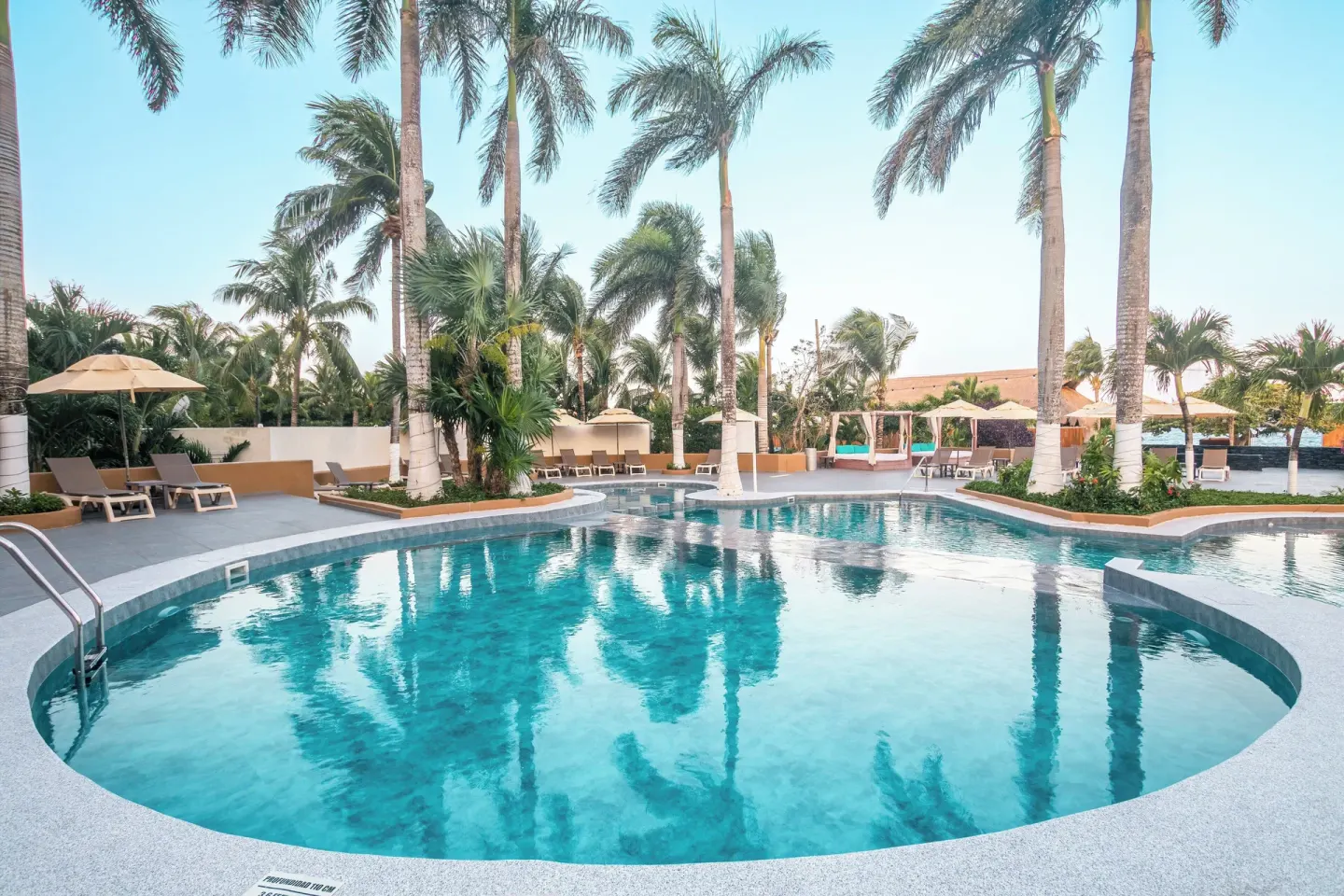 Curved pool with palm trees and loungers at Fiesta Americana Cozumel.