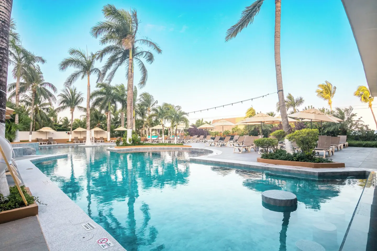 Pool deck with umbrellas, loungers, and palm trees at Fiesta Americana Cozumel.