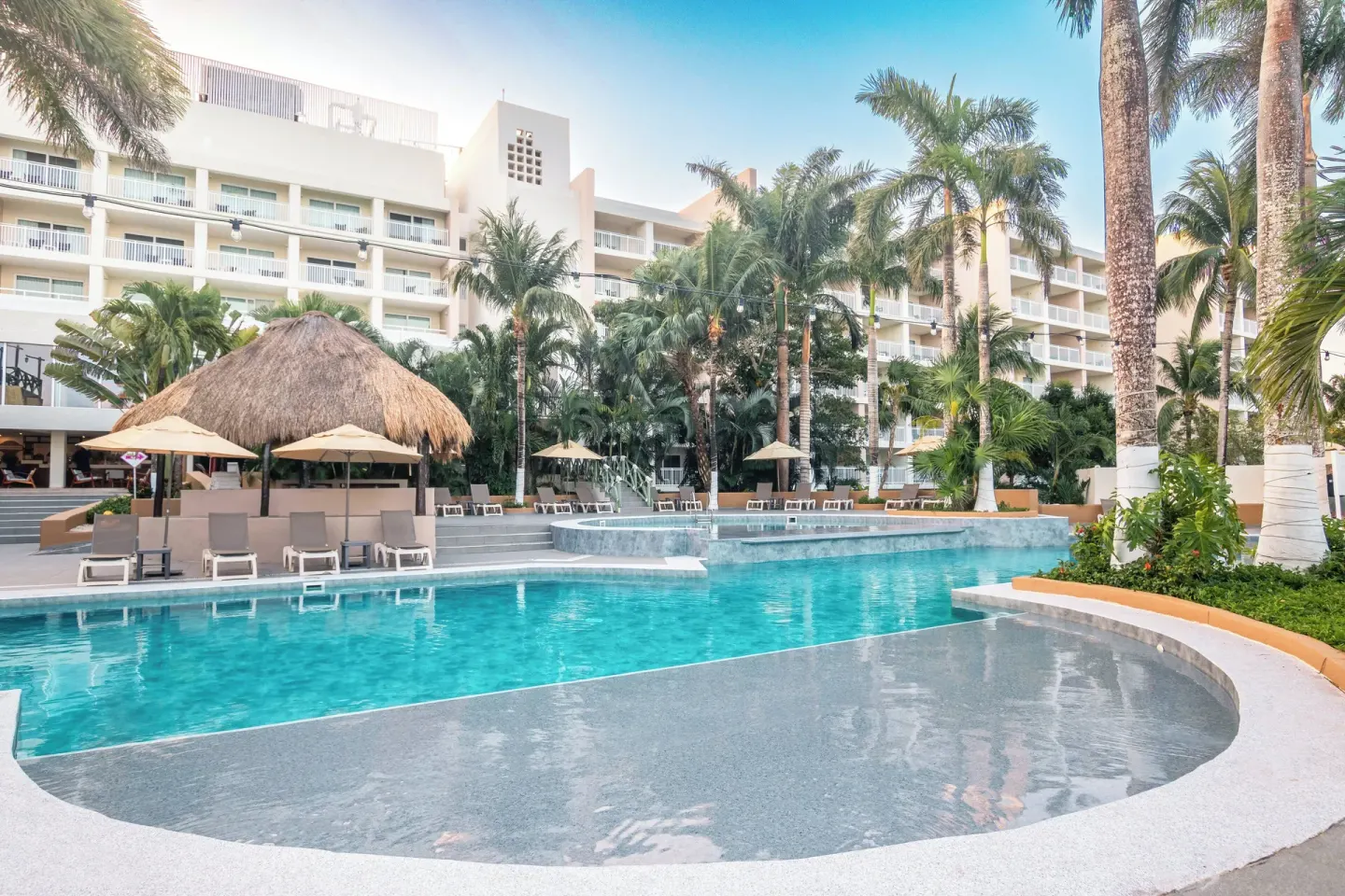 Resort pool, thatched shade structure, and guestroom balconies at Fiesta Americana Cozumel.