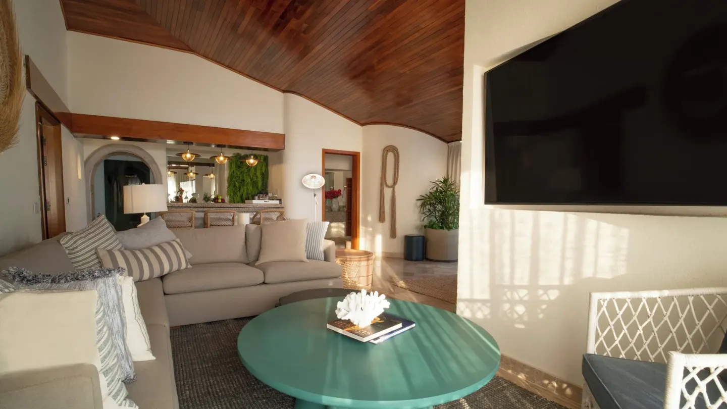 Suite living room with sofa, round table, bar, and wall-mounted TV at Fiesta Americana Puerto Vallarta & Spa.