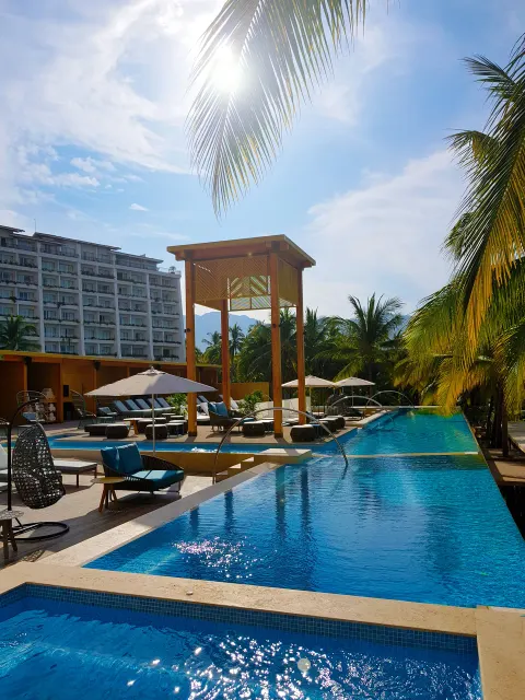 Sunlit pool deck with palms and lounge seating at Fiesta Americana Puerto Vallarta & Spa.