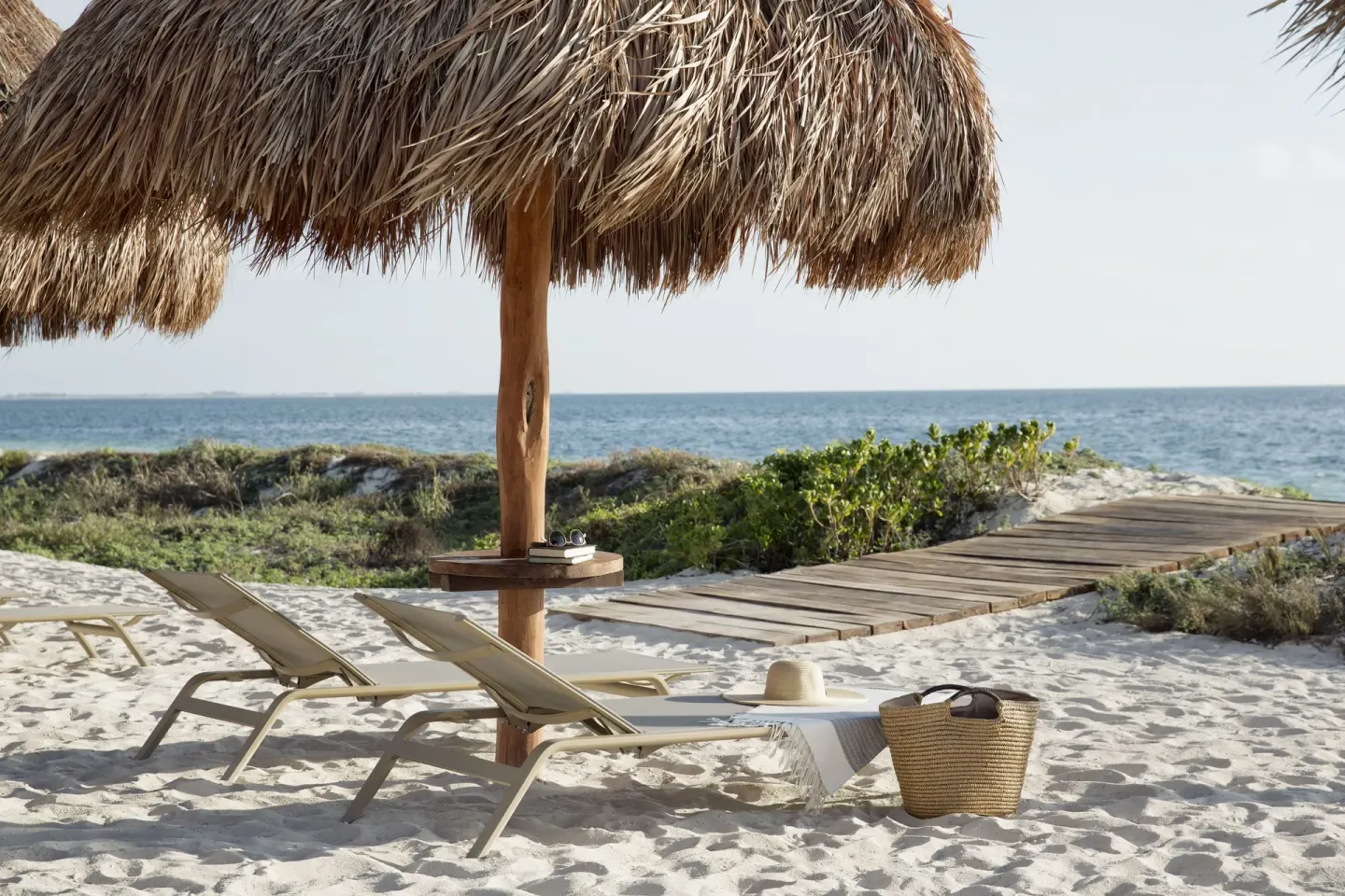 Beach loungers under a thatched palapa beside the sea at Finest Playa Mujeres.