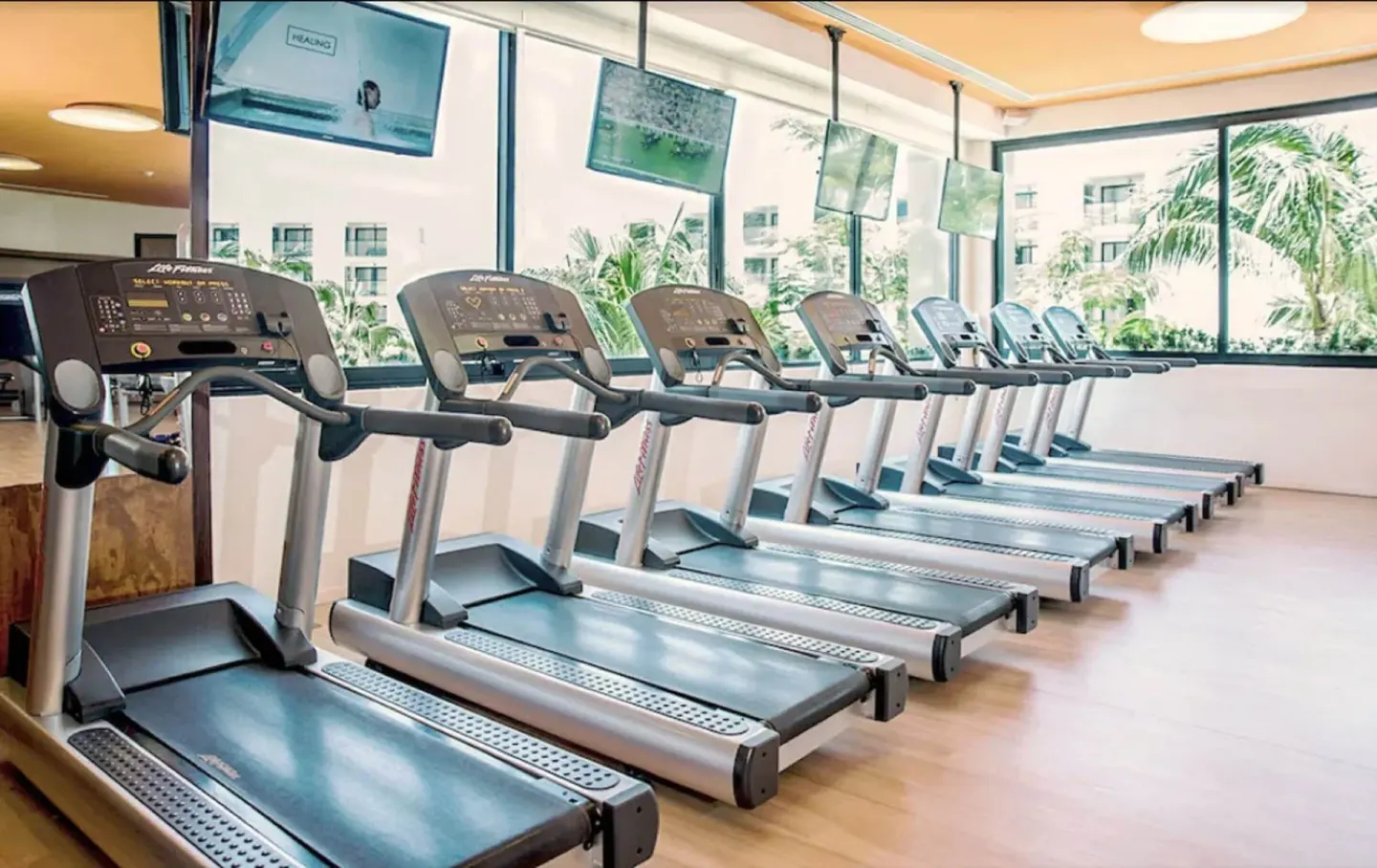 Fitness room with a row of treadmills facing windows at Finest Playa Mujeres.