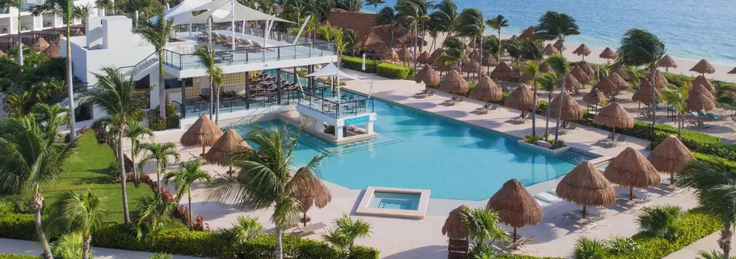 Pool deck with thatched umbrellas and oceanfront beach at Finest Playa Mujeres.