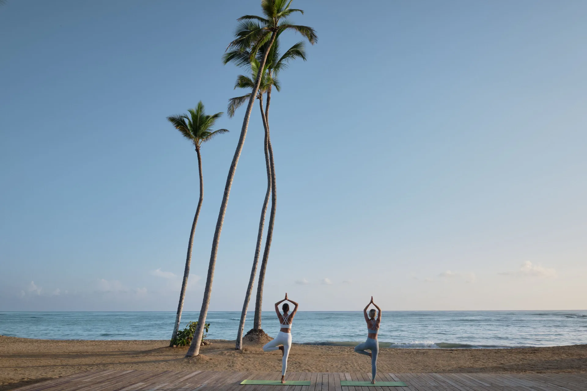Two people doing yoga on the beach beside tall palms at Finest Punta Cana.