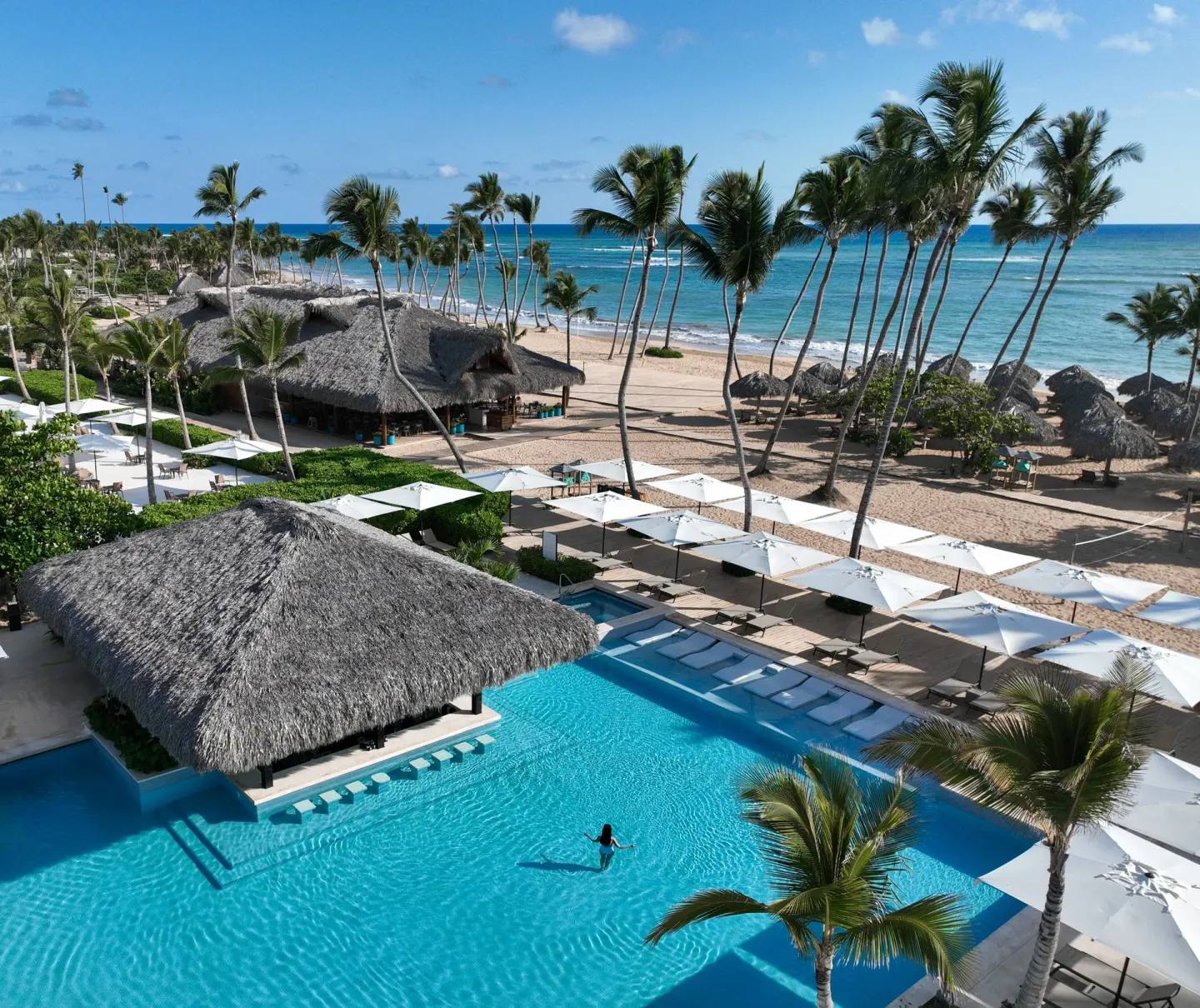 Beachfront pool with palms, umbrellas and ocean at Finest Punta Cana.