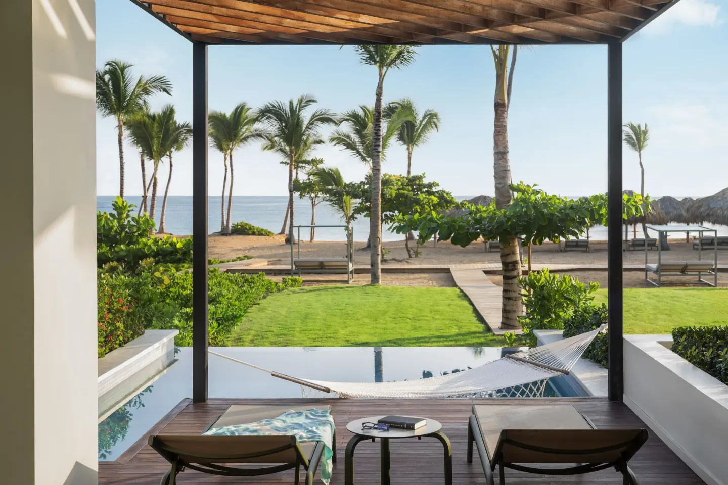 Terrace with loungers, hammock, plunge pool, lawn, palms, and beach beyond at Finest Punta Cana.