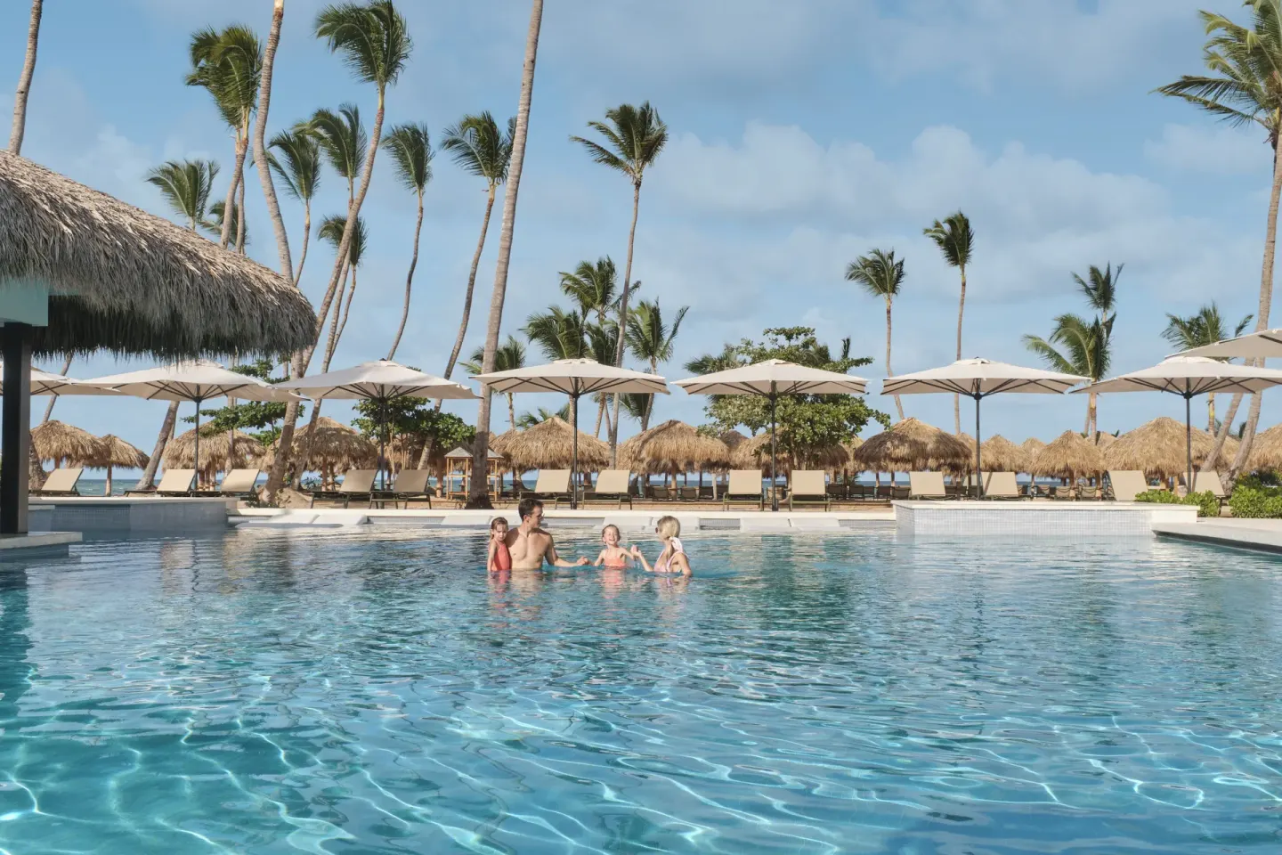Family swimming in a beachside pool with palms and loungers at Finest Punta Cana.