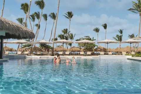 Family swimming in a beachside pool with palms and loungers at Finest Punta Cana.