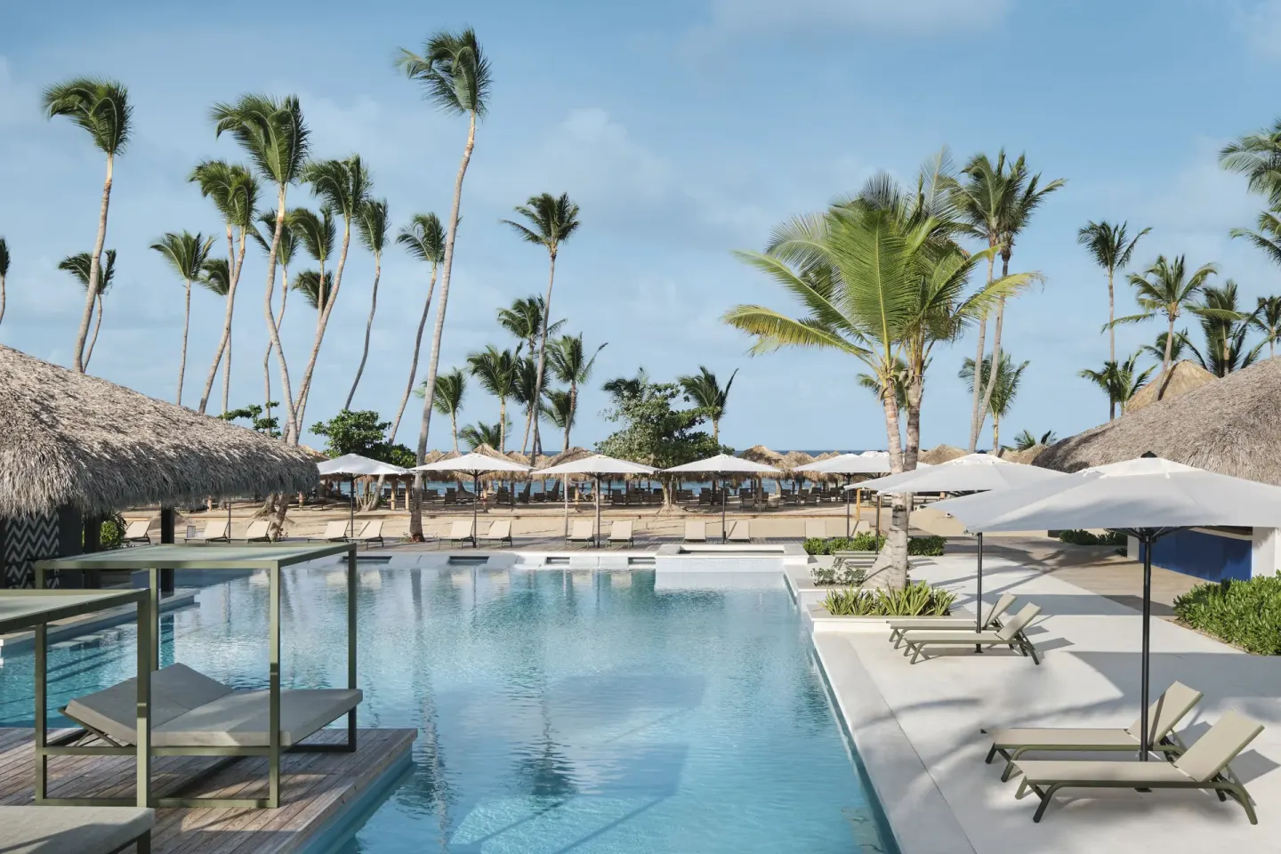 Pool deck with loungers, umbrellas, palms, and beach beyond at Finest Punta Cana.