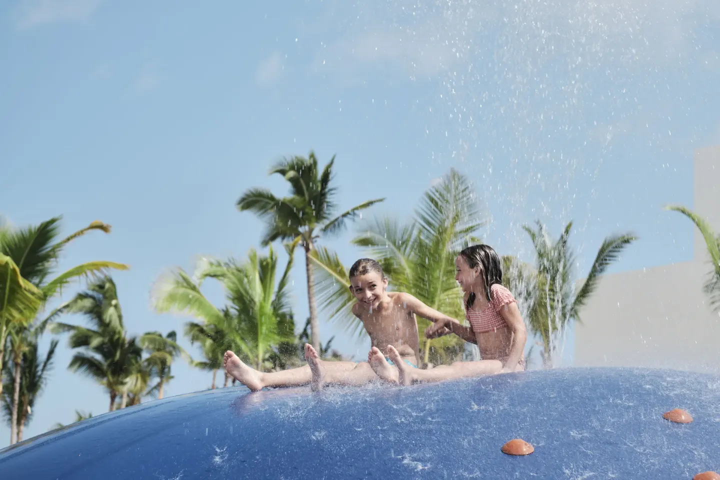 Children sliding through water spray on a blue splash feature at Finest Punta Cana.