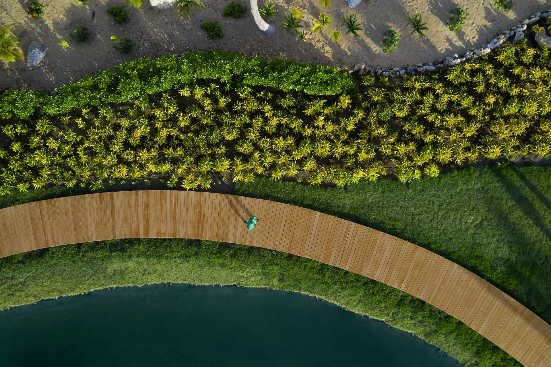 Curved wooden walkway beside gardens and water at Finest Punta Cana.