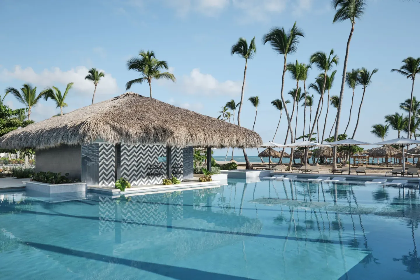 Pool with thatched swim-up bar, palms and ocean beyond at Finest Punta Cana.
