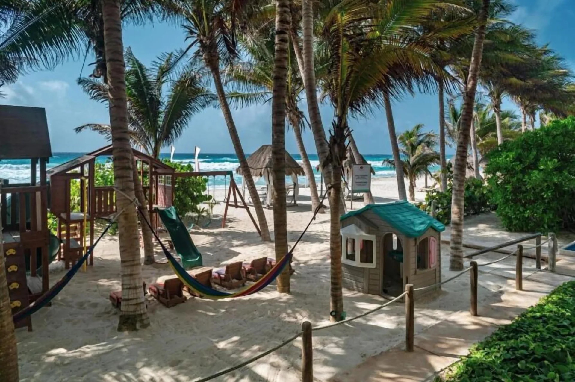 Beachside children's playground with palms, slide, hammock, and playhouse at Flamingo Cancun.