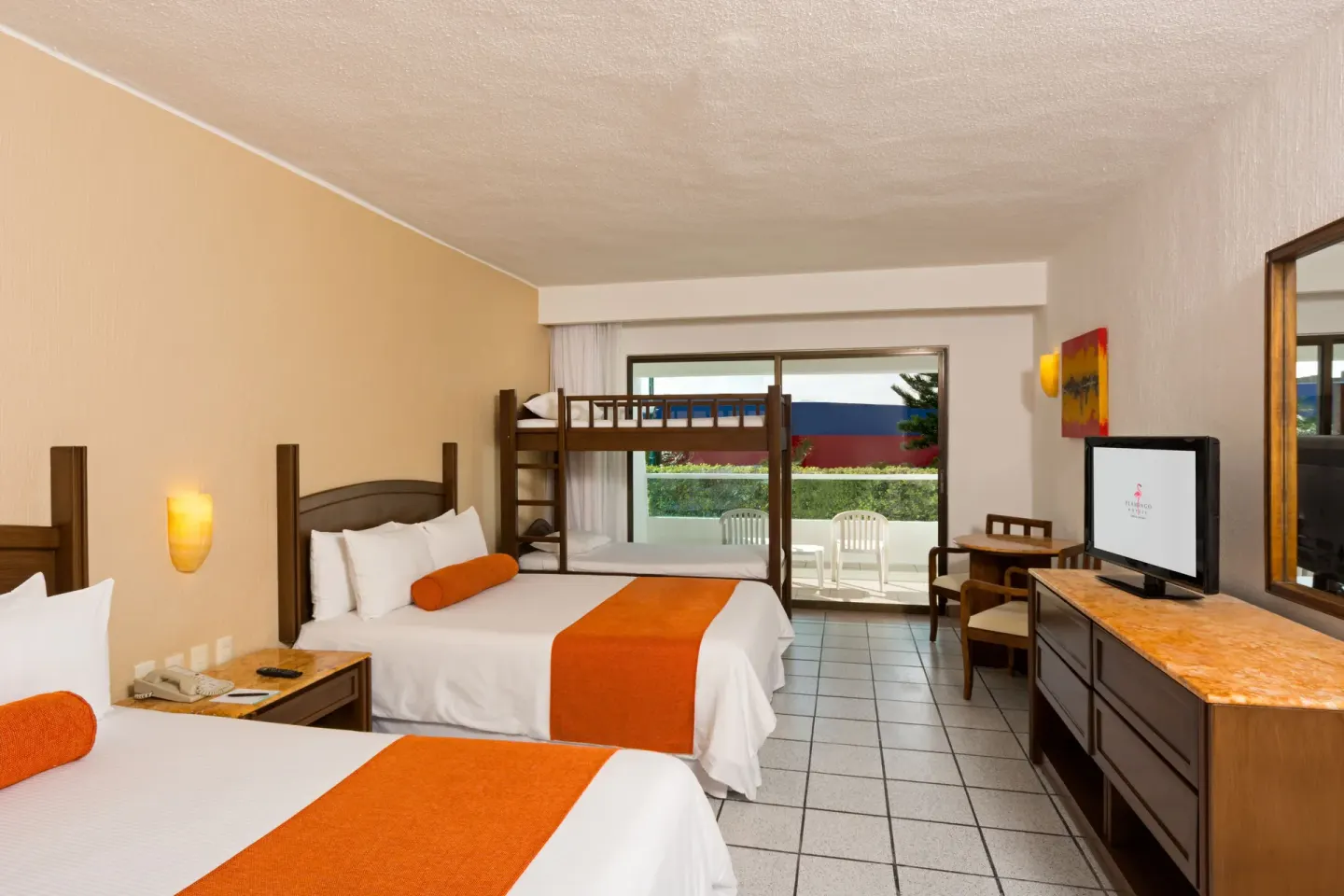 Guest room with two beds, bunk bed, TV, and balcony chairs at Flamingo Cancun.