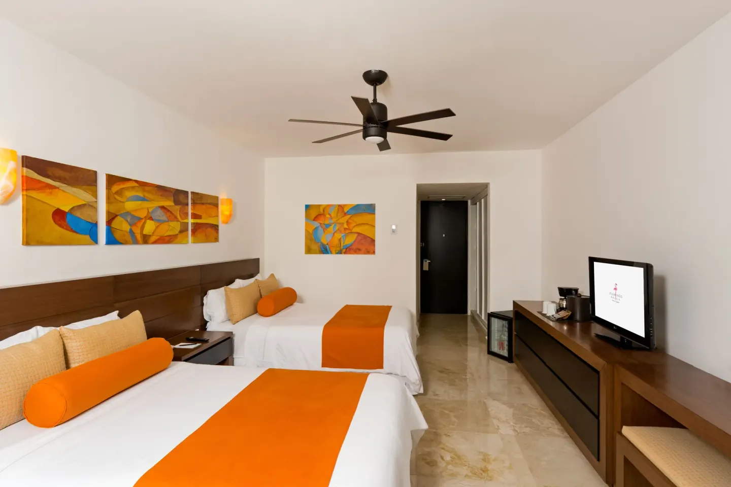Modern guest room with two beds, ceiling fan, and TV console at Flamingo Cancun.