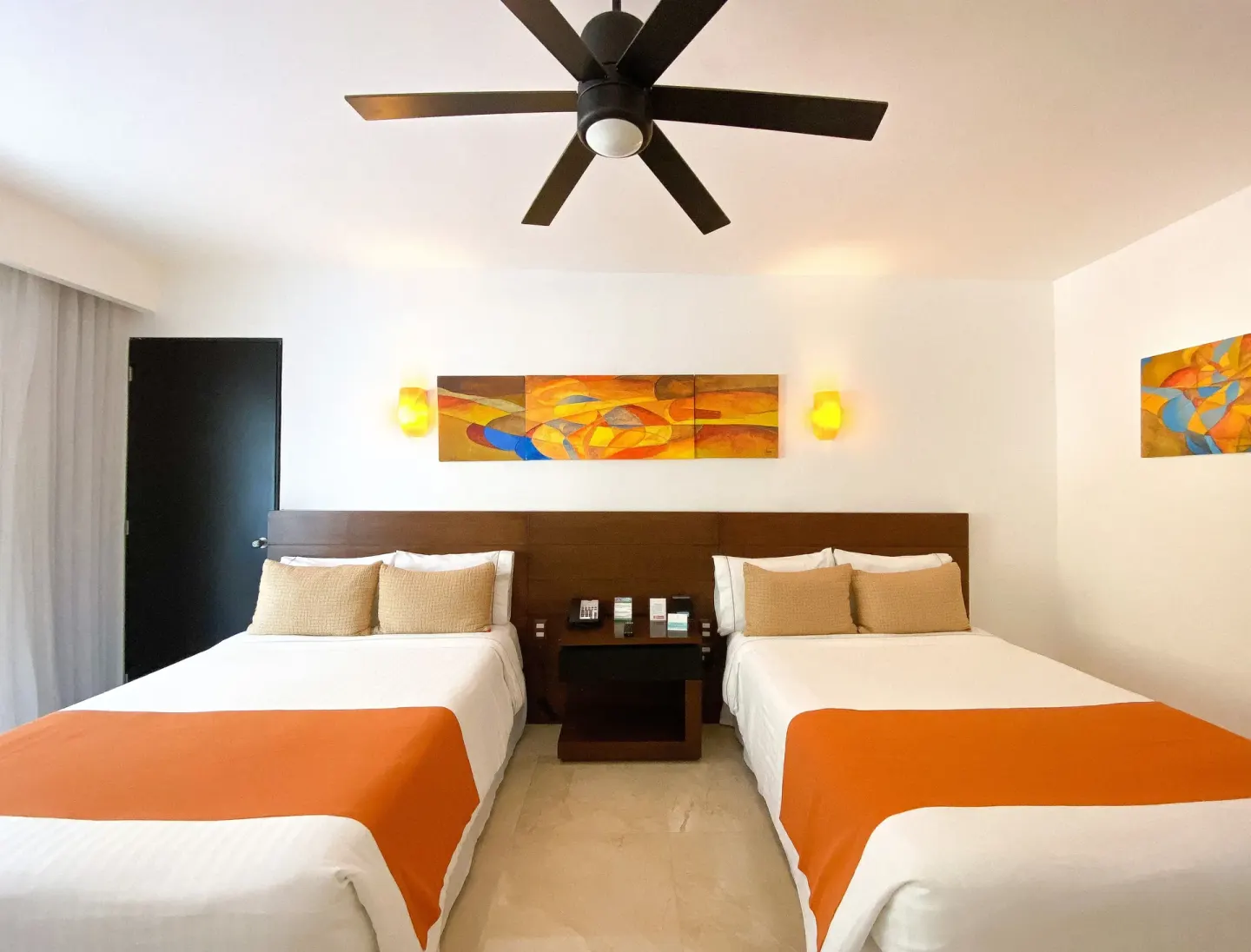 Two beds beneath abstract wall art and a ceiling fan at Flamingo Cancun.