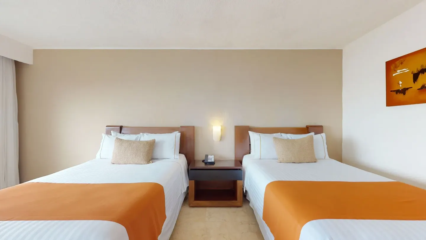 Two beds with orange runners and a shared nightstand at Flamingo Cancun.