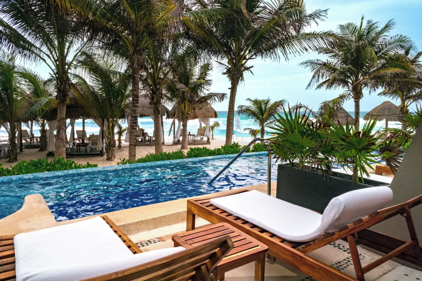 Terrace loungers beside a pool overlooking palms and beach at Flamingo Cancun.
