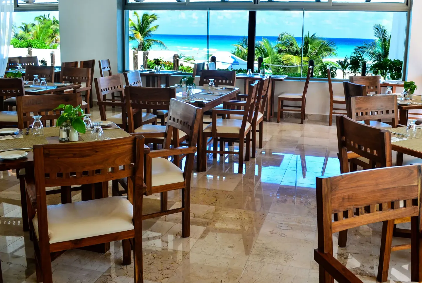 Ocean-view dining room with wooden tables, chairs, and large windows at Flamingo Cancun.