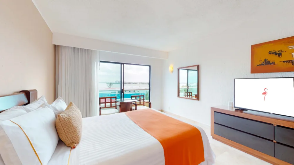 Deluxe Lagoon Room with king bed, balcony seating, and TV at Flamingo Cancun.