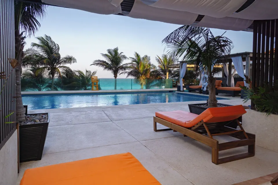 Deluxe Pool Terrace Walkout patio with loungers, pool, palms and ocean at Flamingo Cancun.