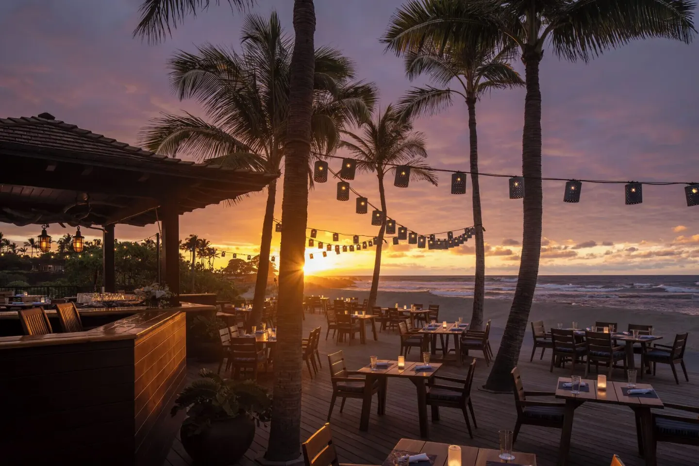 Beachfront dining tables glow at sunset at Four Seasons Resort Hualalai.
