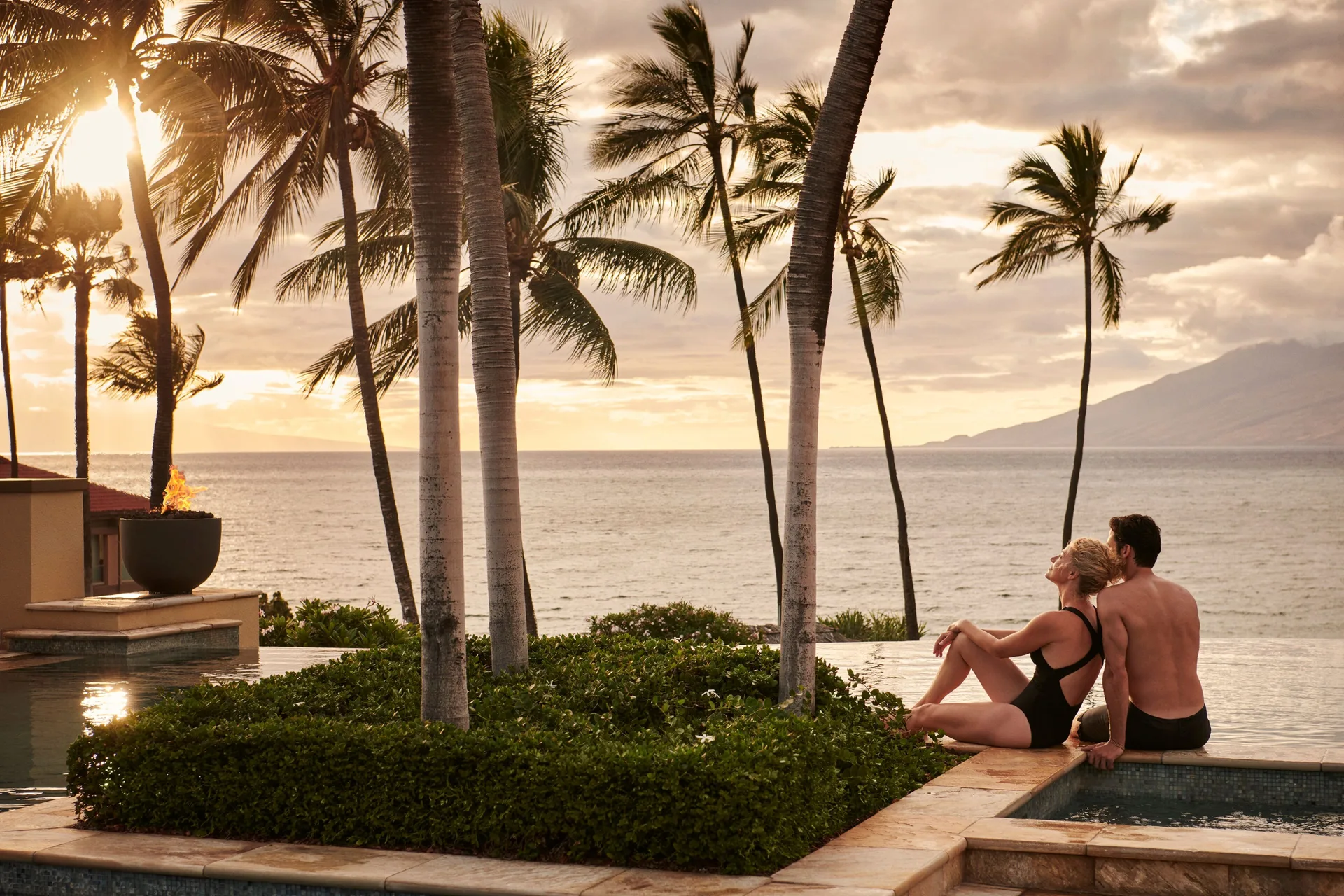 Couple sitting by the pool at sunset at Four Seasons Resort Maui at Wailea.