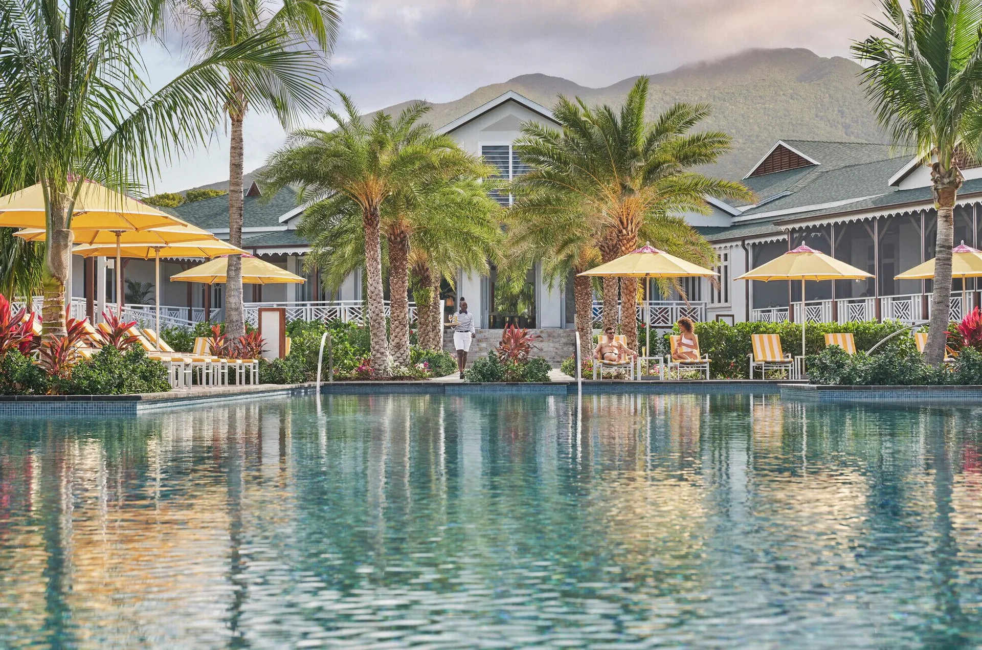 Poolside palms and yellow umbrellas at Four Seasons Resort Nevis with the mountain behind.