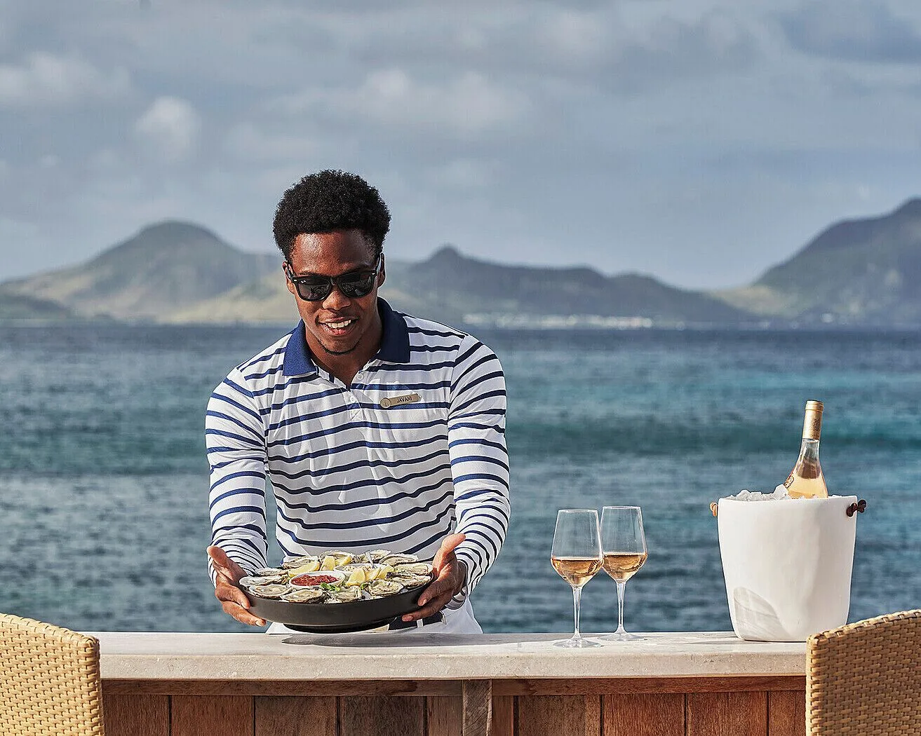 Server presenting oysters and wine by the sea at Four Seasons Resort Nevis.