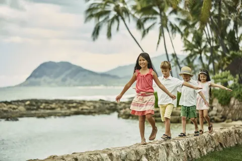 Children walking along a stone seawall at Four Seasons Resort Oahu at Ko Olina.