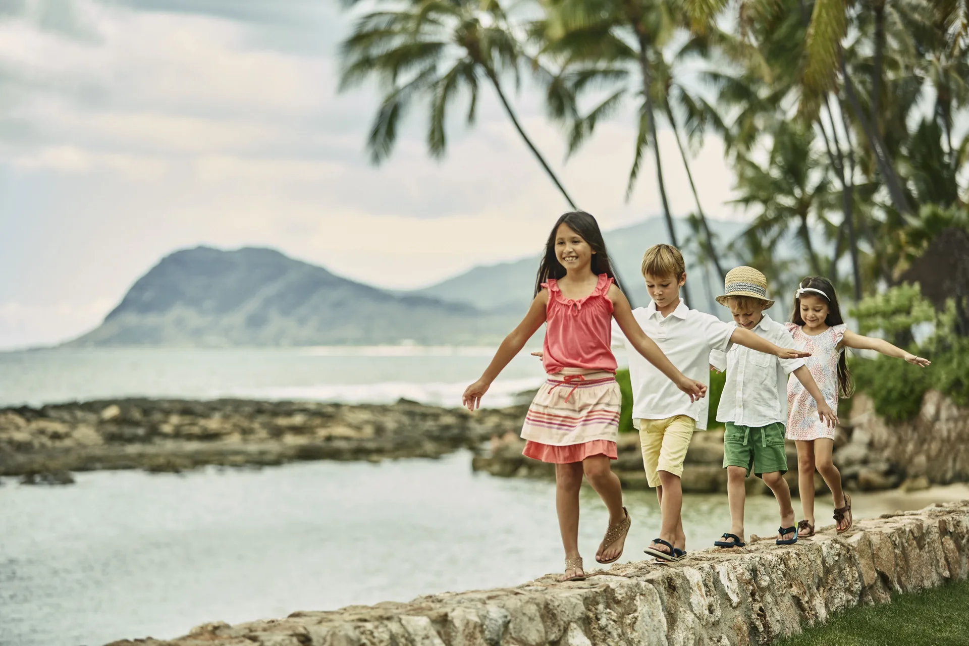 Children walking along a stone seawall at Four Seasons Resort Oahu at Ko Olina.