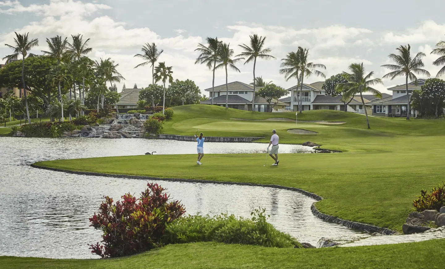 Golfers on a green beside water and palms at Four Seasons Resort Oahu at Ko Olina.
