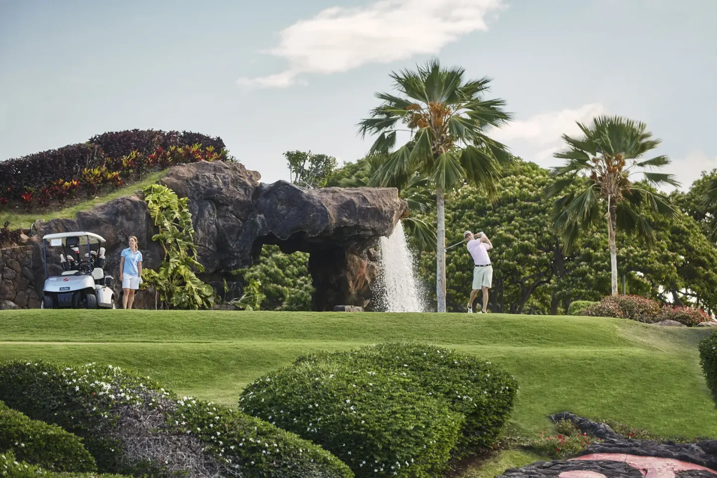 Golfer teeing off near a waterfall and palms at Four Seasons Resort Oahu at Ko Olina.