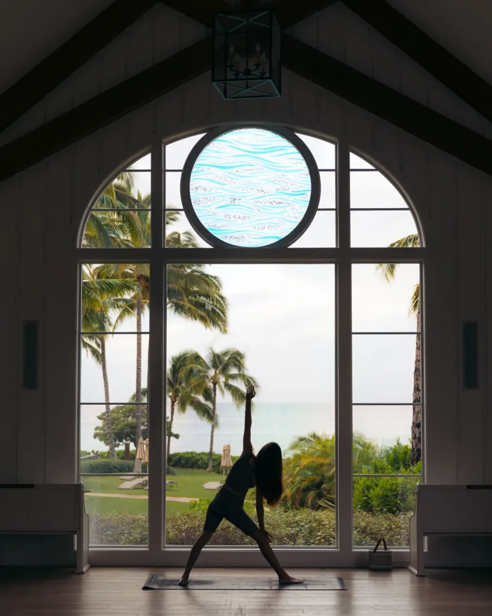 Guest practicing yoga before tall ocean-view windows at Four Seasons Resort Oahu at Ko Olina.